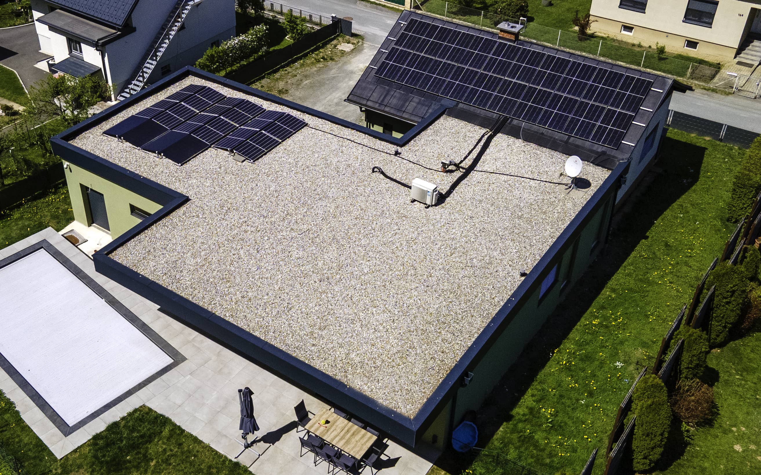 Das Bild zeigt ein Haus aus der Vogelperspektive. Im vorderen Teil sieht man das neu errichtete Flachdach mit PV-Modulen. Im hinteren Bereich des Bildes sieht man den Altbestand samt Satteldach und montierten PV-Modulen.