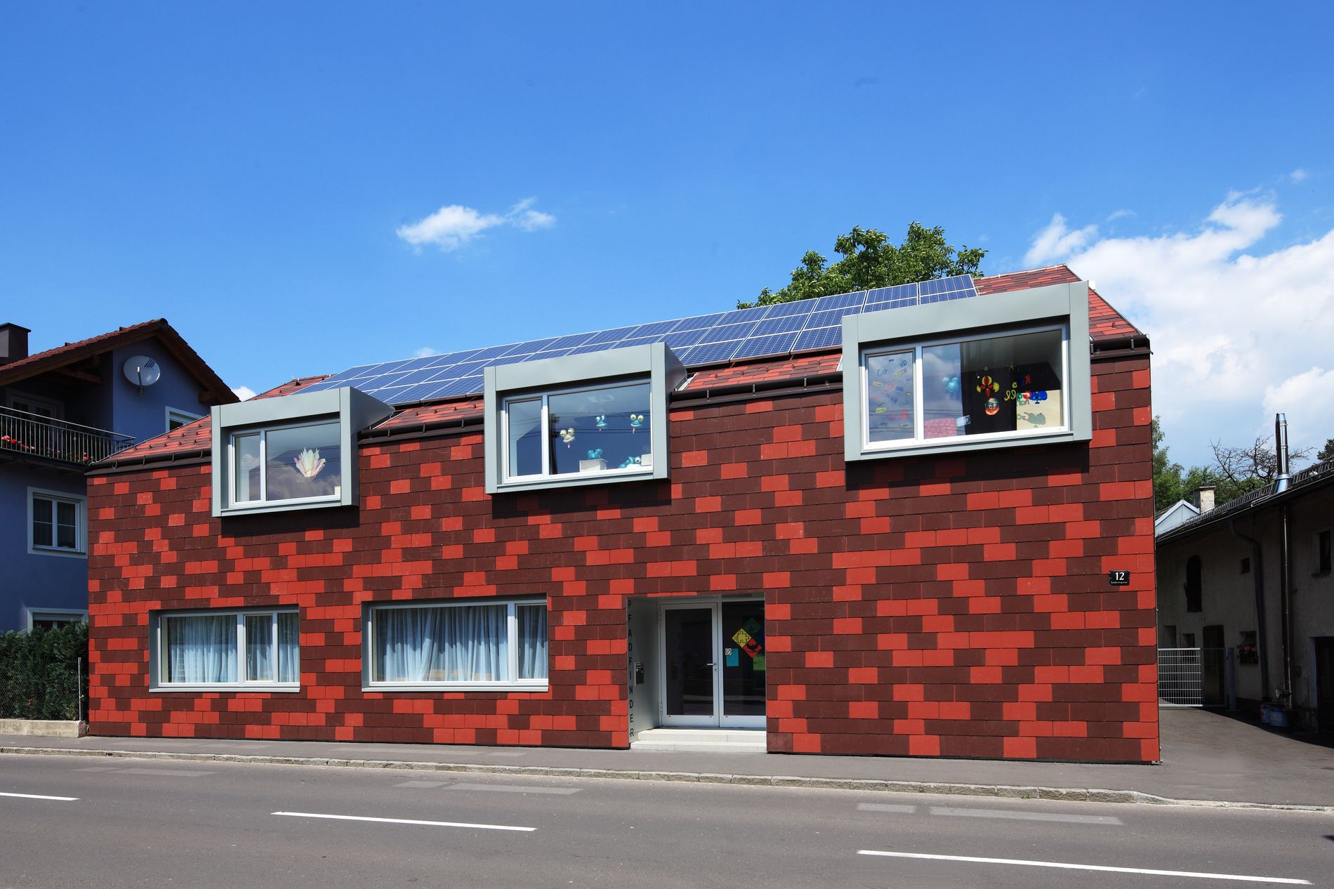 Modernes Gebäude ummantelt von einer fassaden aus Eternit mit verschiedenen Rottönen.
