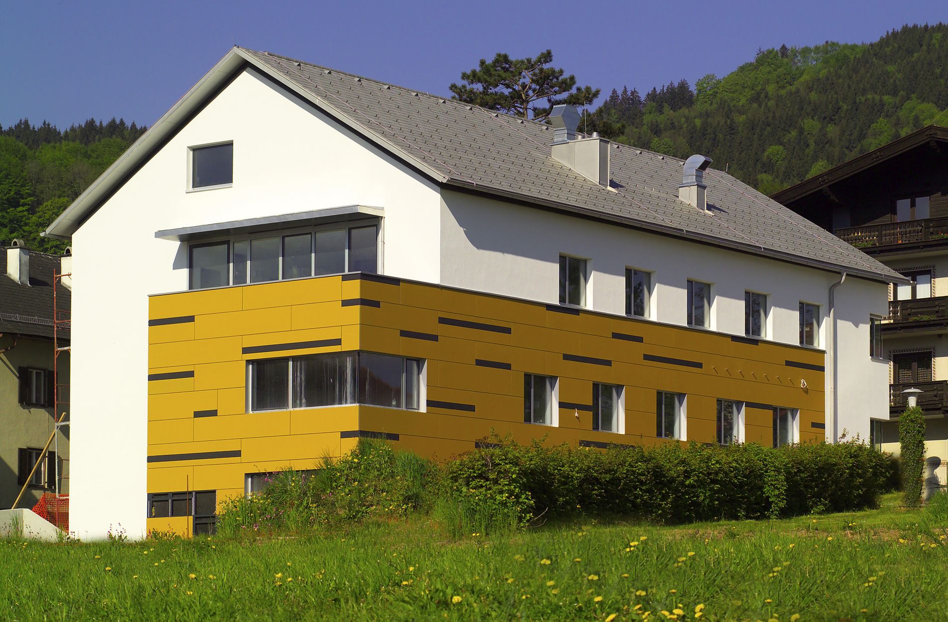 Modernes Einfamilienhaus mit hellgrauem Satteldach sowie einer gelben Fassaden aus Eternit.