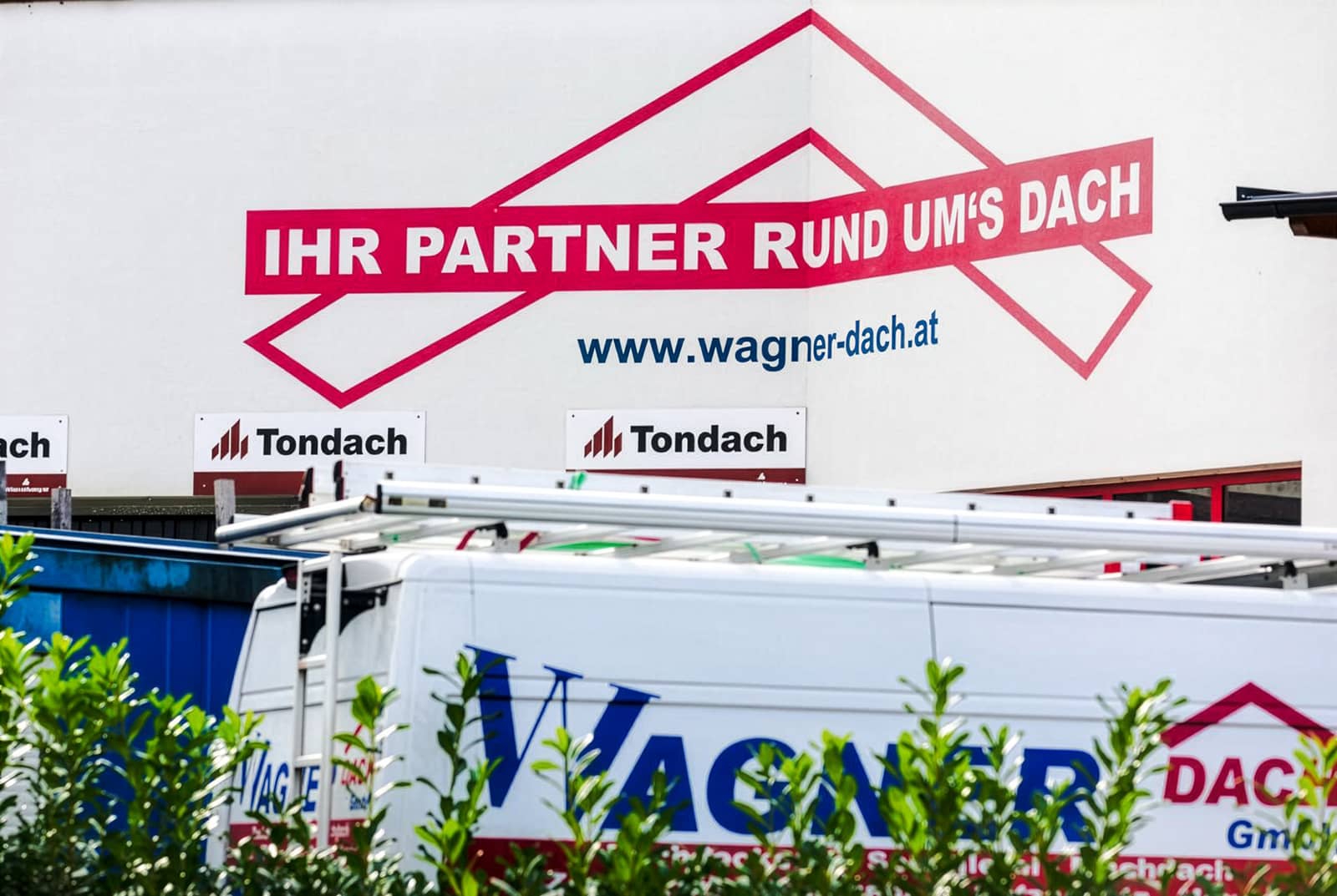 DAs Bild zeigt eine Fassade mit dem Logo von Wagner Dach und dem Spruch "Ihr Partner rund ums Dach".